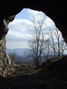 bare trees viewed from dome shaped rock opening under blue sky during daytime thumbnail