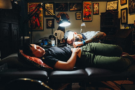 man performing tattoo operation in man lying on bed thumbnail