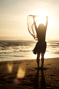 woman holding scarf standing on beach shore during sunset thumbnail