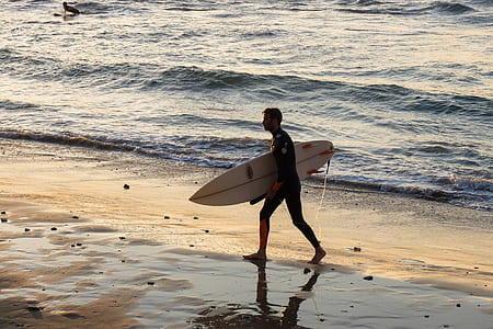 man carrying white surfboard while walking on shore during daytime thumbnail