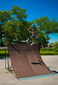 Man Playing Scooter on Top of Brown Wooden Skateboard Ramp thumbnail