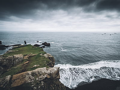 person standing on cliff near body of water thumbnail