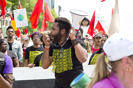 standing man using megaphone surrounded by people holding flags thumbnail