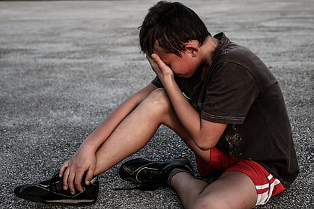 boy in brown shirt and red gym shorts sitting on concrete floor thumbnail