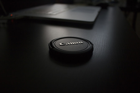 black Canon camera lens cover on brown wooden board thumbnail