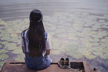 woman sitting on brown wooden dock beside pair of gray low-top sneakers thumbnail