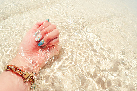 person hands  wearing gold bracelet and white-blue nail polish on body of water thumbnail