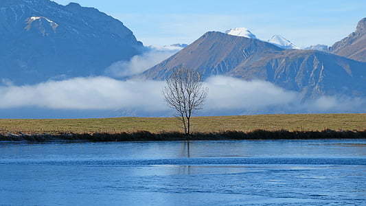 body of water near mountain range beside grass field thumbnail
