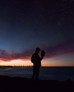 silhouette of man standing while holding his hat during nighttime thumbnail