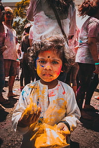 girl stained with yellow powder standing in front of crowd thumbnail
