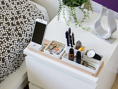 silver iPhone 6 on white holder beside coins and pens on white wooden nightstand thumbnail