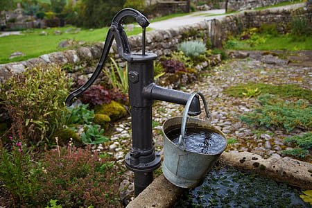 gray steel bucket filled with water hanging on manual water pump thumbnail