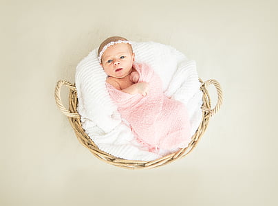 baby covered by pink swaddle on round brown wicker basket thumbnail