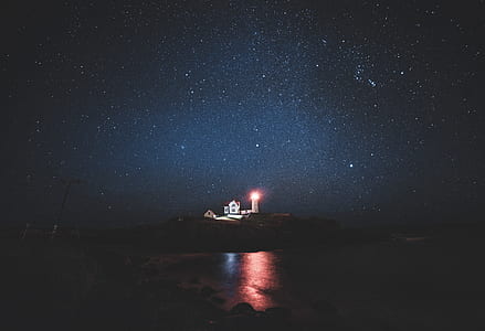 photography of lighthouse and house during nighttime thumbnail