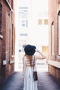 woman holding hat standing between buildings thumbnail