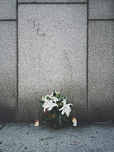 white petaled flowers in vase between lit candles in front of concrete wall thumbnail