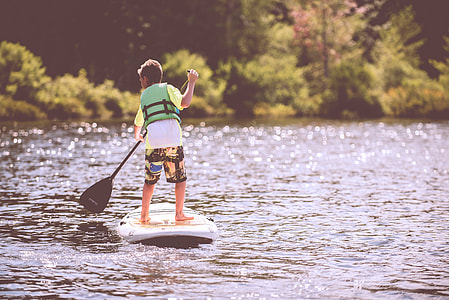 boy in green vest on white and black paddle boat on body of water during daytime thumbnail