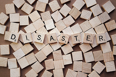 brown wooden scrabble tiles forming disaster word on top of other scrabble tiles thumbnail