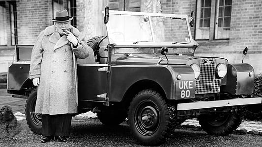 grayscale photo of man in front of vehicle wearing button-up coat thumbnail