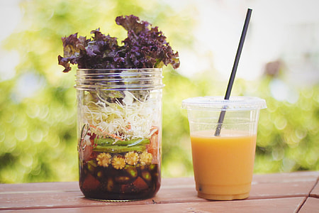 clear plastic cup with juice and strap beside clear glass jar with flower during daytime thumbnail