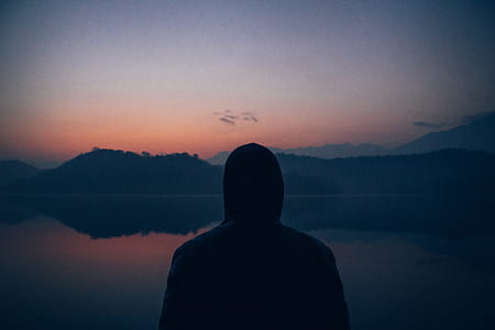 person in hoodie standing near body of water thumbnail