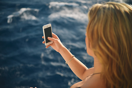 woman holding silver iPhone 5s in front of her face at body of water thumbnail