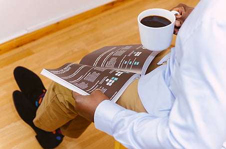 man reading magazine while standing and holding a white mug thumbnail