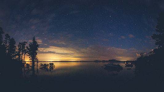 white powerboat on body of water heading towards trees during golden hour thumbnail