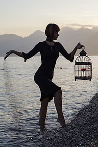 woman wearing black long-sleeved dress holding black metal birdcage thumbnail