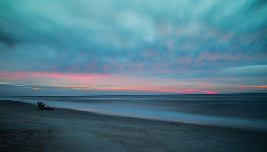 person sitting on gray sand near sea during dawn thumbnail