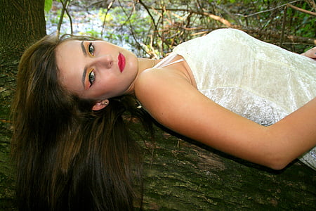 woman wearing white floral sleeveless dress lying on tree trunk during daytime thumbnail