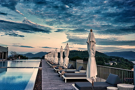 lounge chairs with patio umbrella beside swimming pool near body of mountains thumbnail