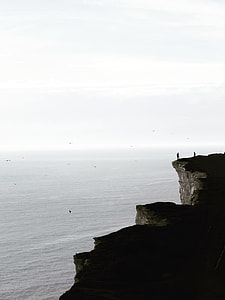 two people standing on cliff near body of water thumbnail