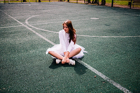 woman wearing white dress sitting on basketball court during daytime thumbnail