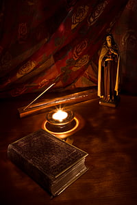 religious figurine near lighted candle and book on brown table thumbnail
