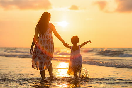 woman wearing white and red sleeveless dress walking with girl on sea shore during sunset thumbnail
