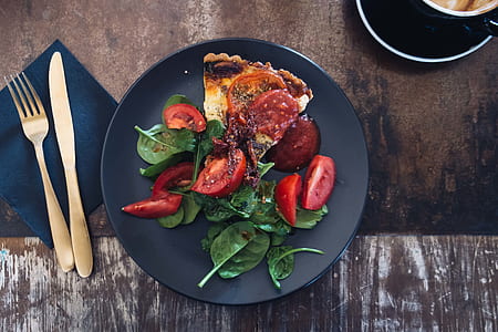 red sliced tomatoes and green leaves on round black plate thumbnail
