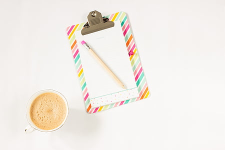 top-view photograph of clipboard, pencil, and cup filled with liquid thumbnail