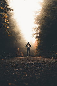 person standing in the middle of the road with green trees thumbnail