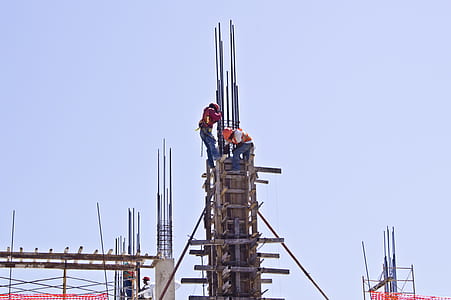 two men filling cement in building's post during daytime thumbnail