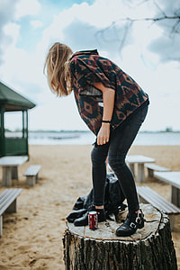 Beautiful blonde woman relaxing with a can of coke on a tree stump by the beach thumbnail
