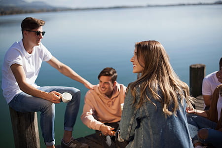woman wearing gray denim jacket sitting on wood dock facing right with four other people during daytime thumbnail
