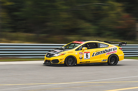 yellow stock car on road near gray fence thumbnail