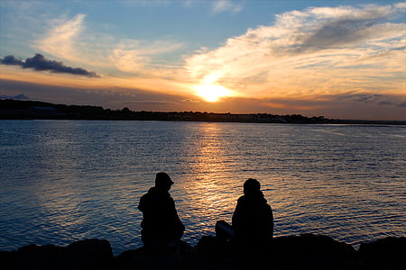 silhouette photo of two man sitting in front of body of water thumbnail