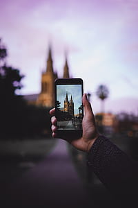person holding black smartphone while taking a picture of brown castle during daytime thumbnail