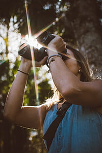 woman using black binocular under tree during day time thumbnail