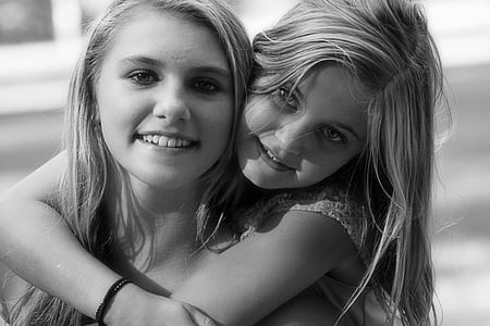 grayscale photography of girl carrying another girl wearing cap-sleeved top thumbnail