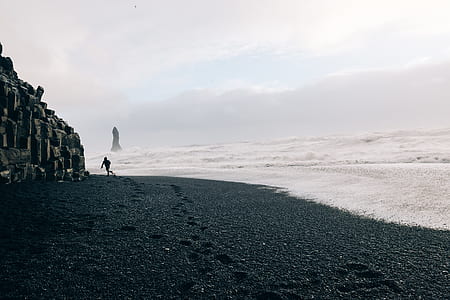 person walking on shore with calm waves during daytime thumbnail