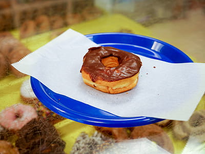 Chocolate donut sitting on a blue plate in a donut shop. thumbnail