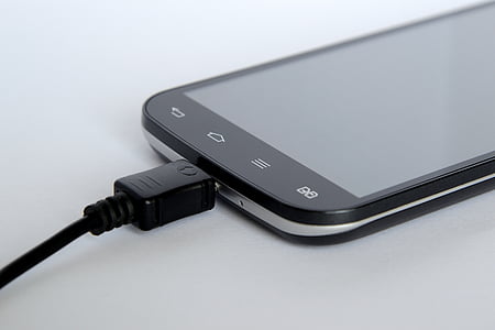 charging black Android smartphone on white surface thumbnail